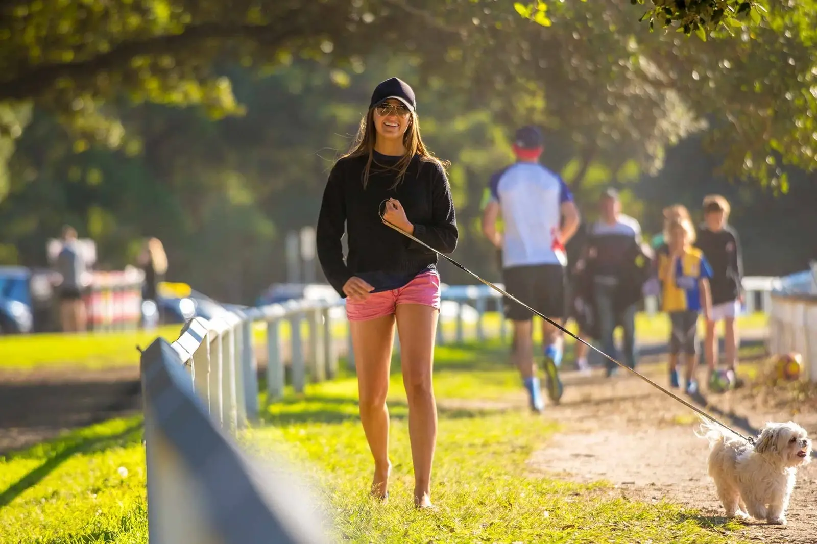 A woman smiles at the camera as she walks her dog in Centennial park Sydney